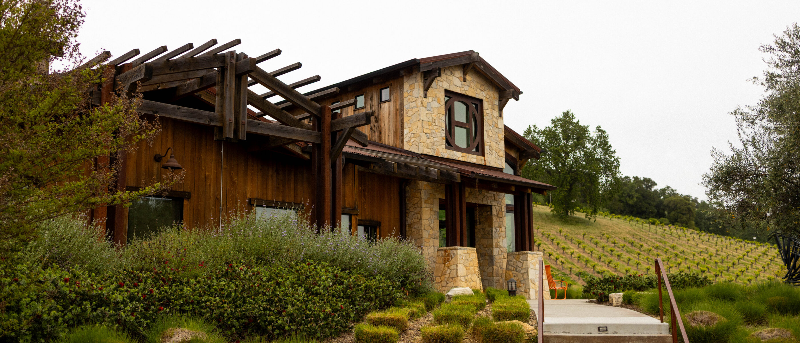 A rustic-style building with wooden and stone elements, surrounded by landscaped greenery and steps leading to the entrance.