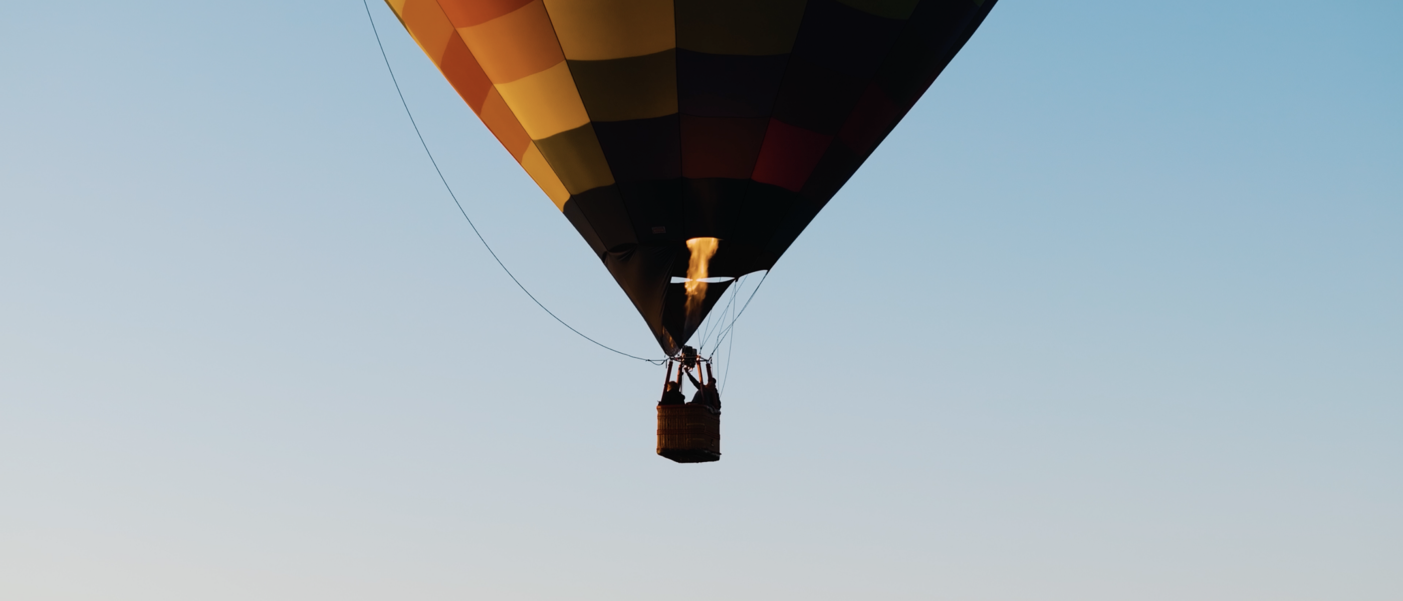 A colorful hot air balloon floats against a clear blue sky. The balloon features a checkered pattern in warm colors.