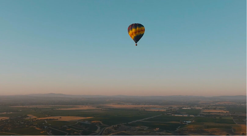 A colorful hot air balloon is floating in a clear blue sky above a vast, open landscape.